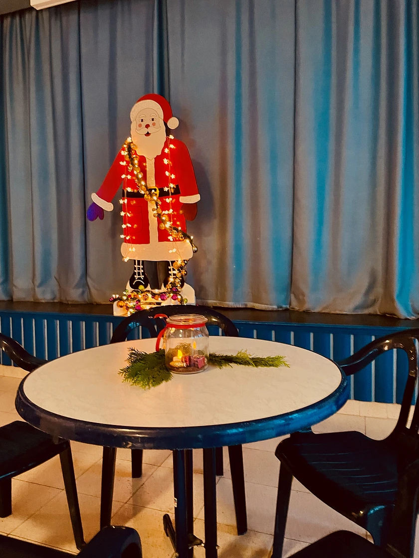 Das Foto zeigt einen Tisch mit Stühlen in der Schulaula. Der Tisch ist weihnachtlich dekoriert. Im Hintergrund steht auf der Bühne eine Weihnachtsmannfigur mit Lichterkette