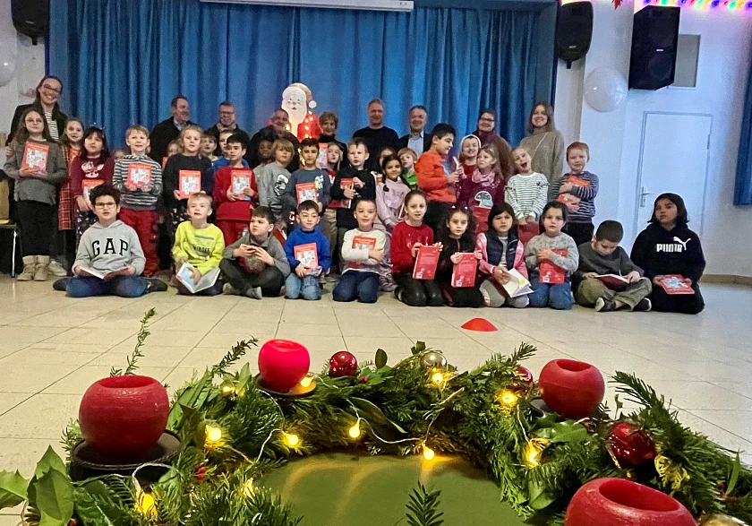 Gruppenbild mit vielen Personen in der Aula. Kinder halten Mein erstes Buch in den Händen. Im Vordergrund ist ein Adventskranz zu sehen